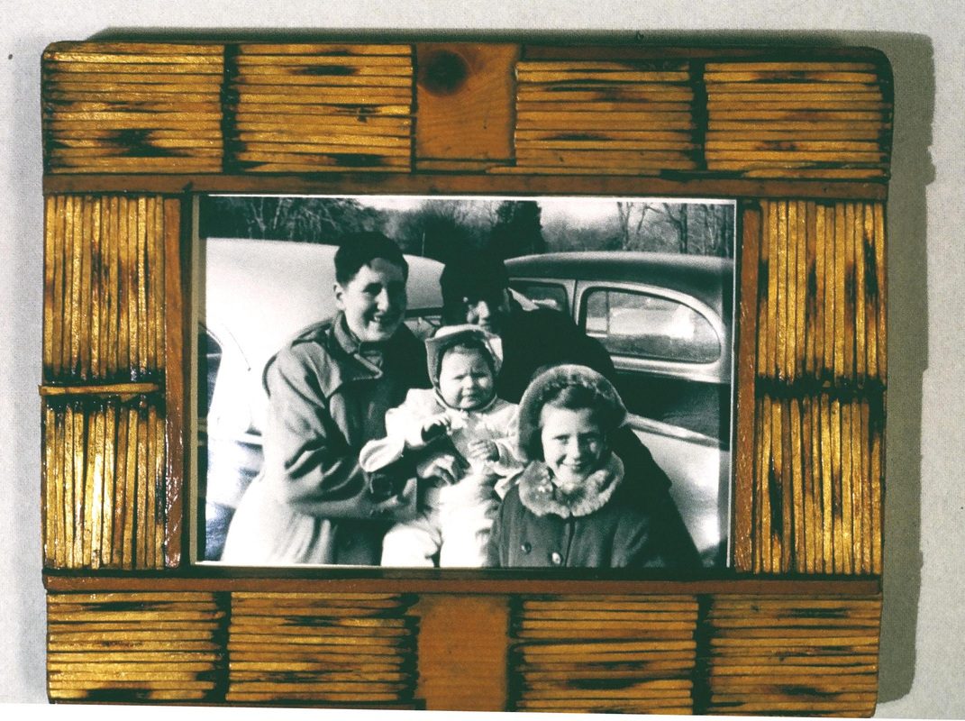 A picture of two people and a baby in front of an old car.