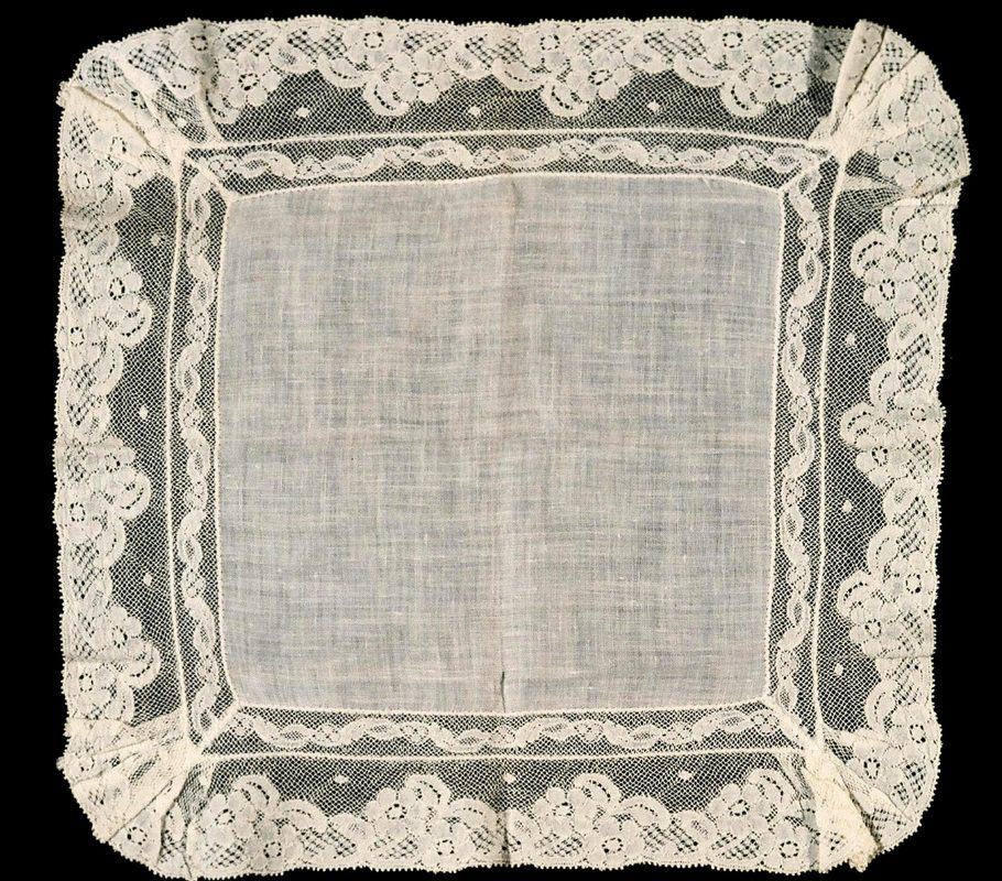 A square white cloth with lace on top of it.